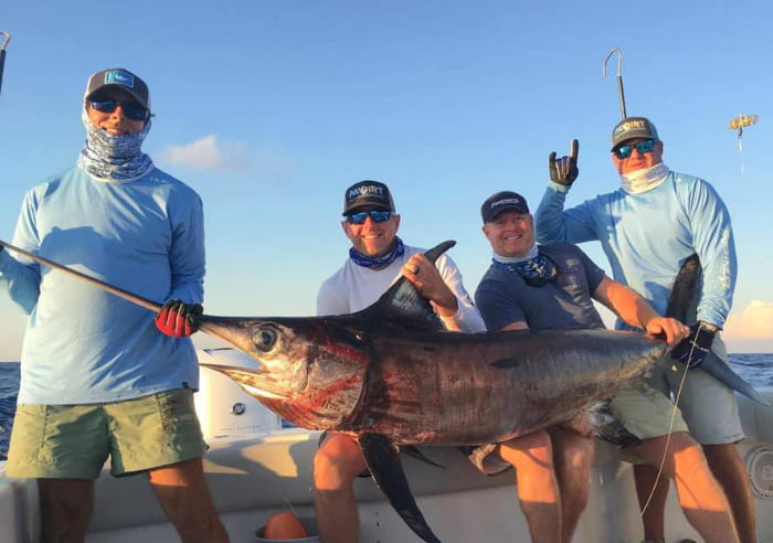 4 men holding a huge sword fish